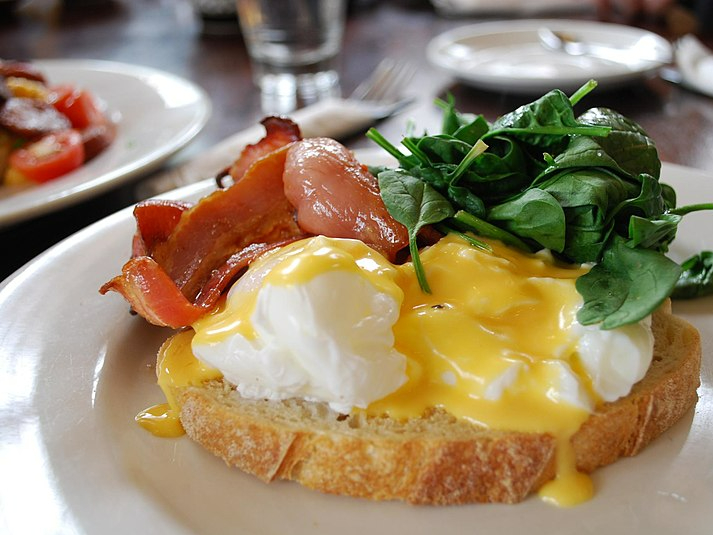Eggs Benedict with bacon and spinach on a table with other dishes in the background